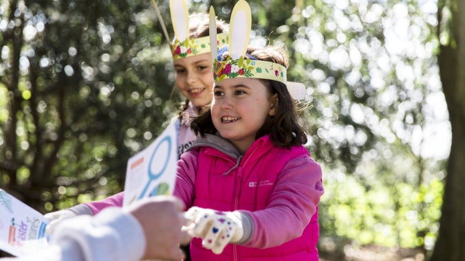 A little girl in a bright pink coat wearing paper bunny ears receiving an Easter trail at a National Trust property